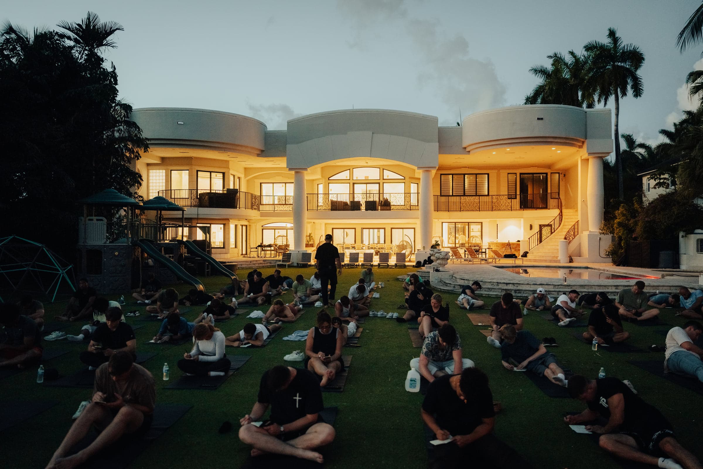 A large group seated on the lawn of a private estate glowing in the evening light