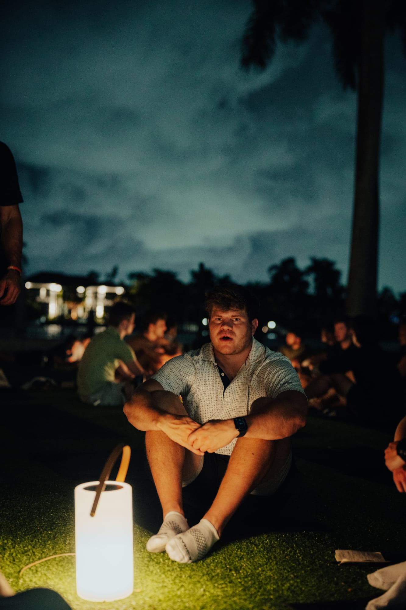 Participants seated around a glowing lantern at night, sharing reflections in a small circle