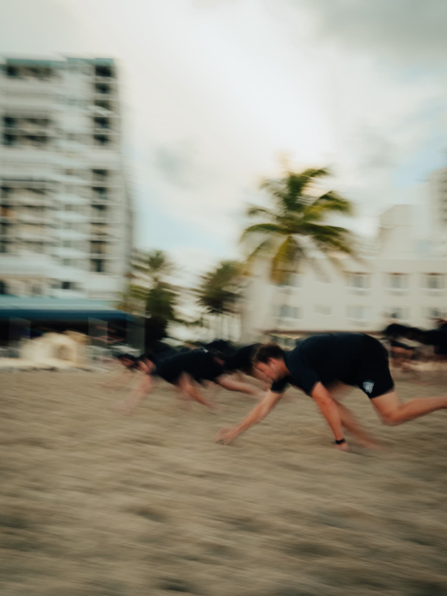 Motion-blurred participants bear-crawling across the sand during a beach activation