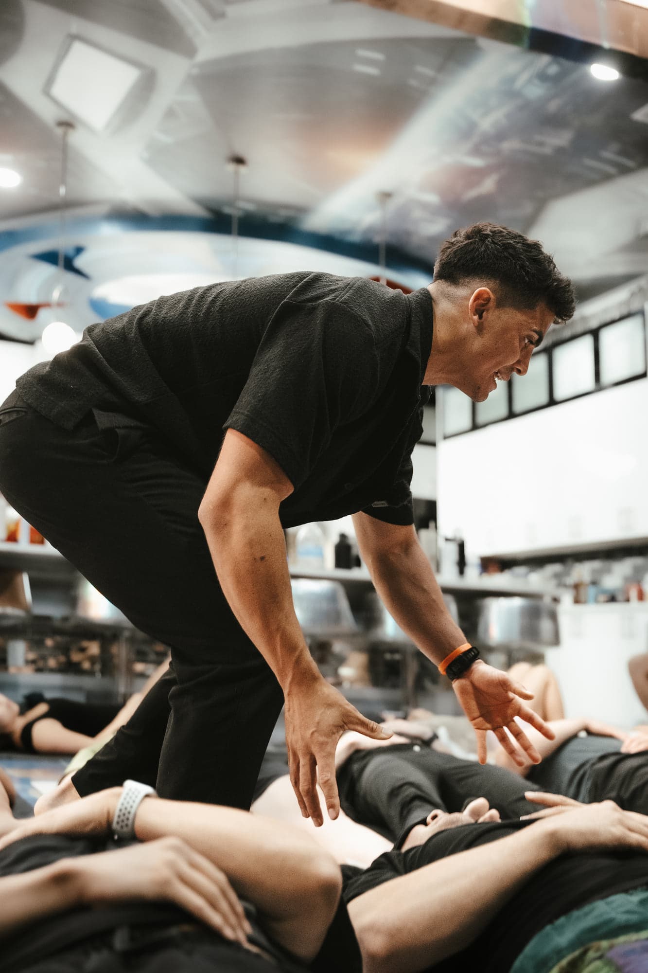 Jovany Ruiz leaning over to guide a participant lying on a mat during an indoor breathwork session