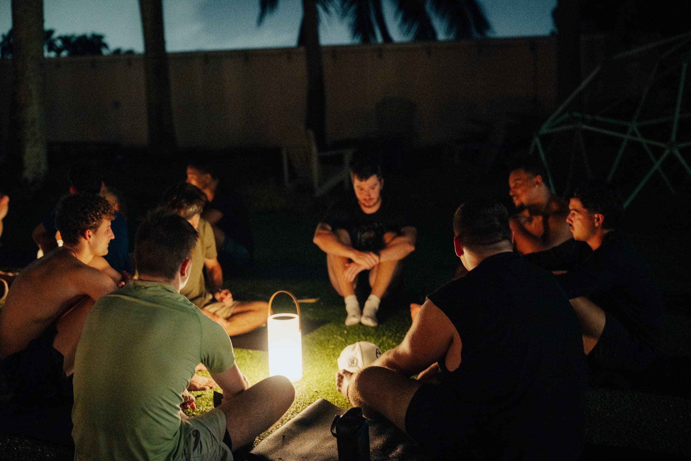 A small group seated around a lantern at night, deep in conversation